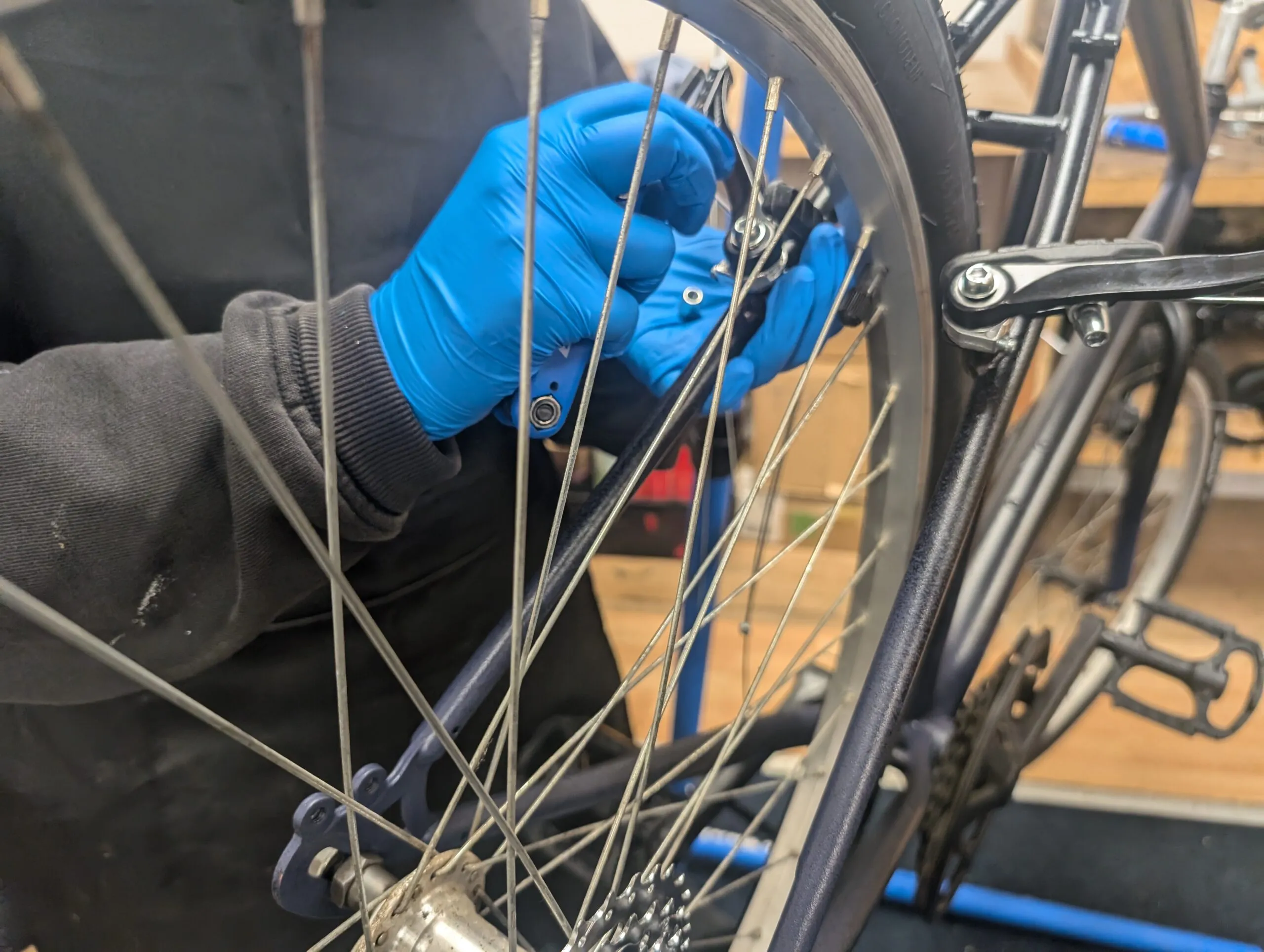 A close up shot of a persons hands fixing a spoke of a bicycle wheel.